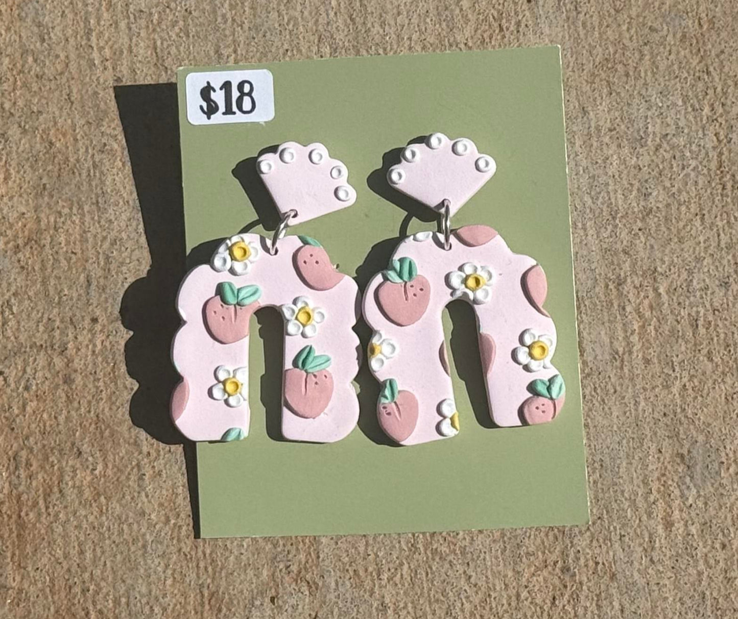 Pair of earrings on a green card with a price tag on a beige surface