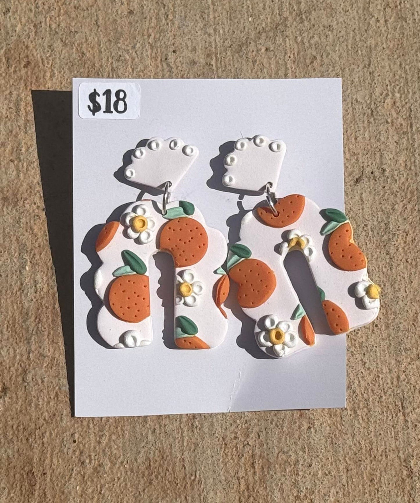 Pair of earrings with floral design on a white card with price tag, placed on brown surface.